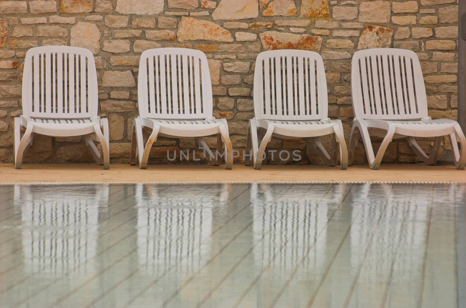 White plastic seats standing on a terrace next to a pool