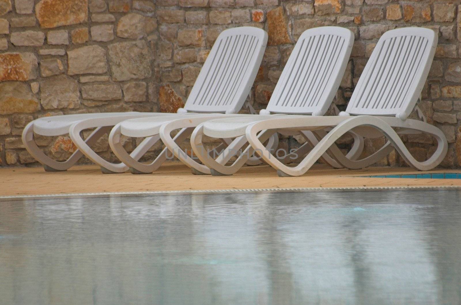 White plastic seats standing on a terrace next to a pool