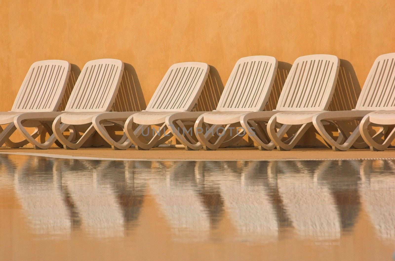 White plastic seats standing on a terrace next to a pool