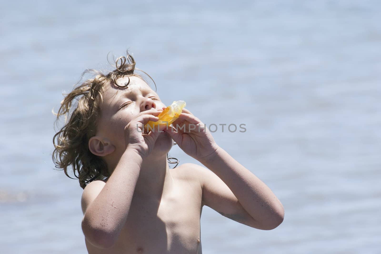 Face to the sun, a boy enjoys a cool ice block after a summer swim.