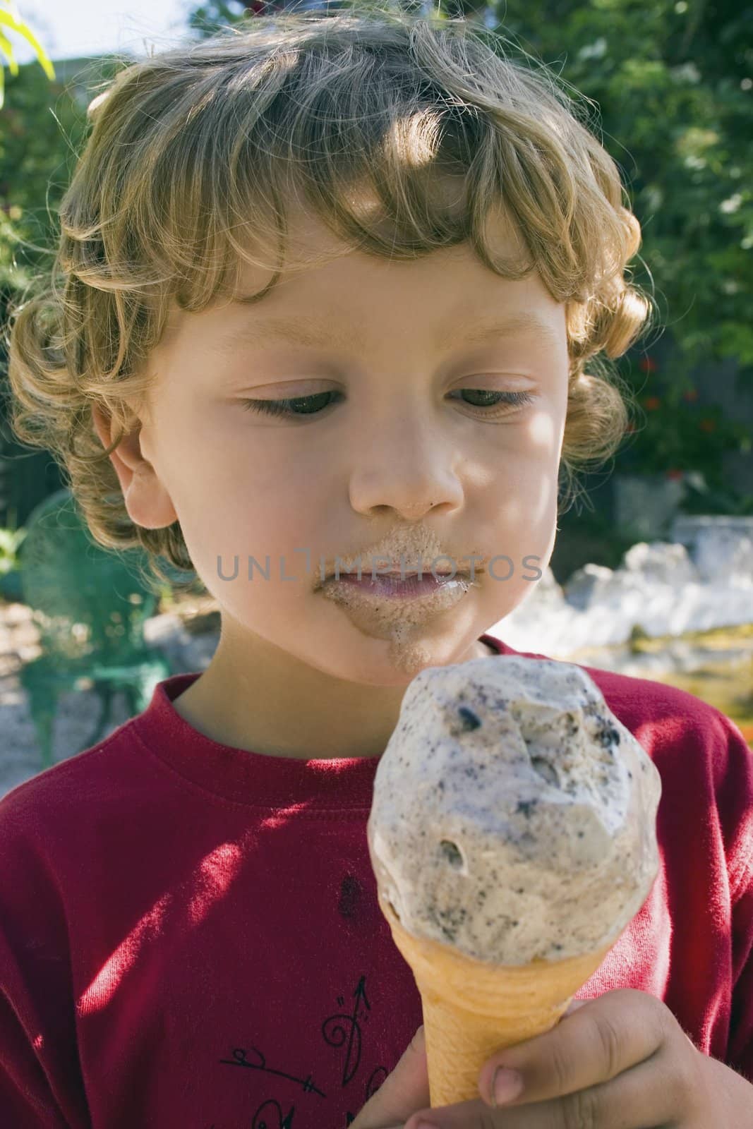 A boy eats an ice cream while shading under a tree