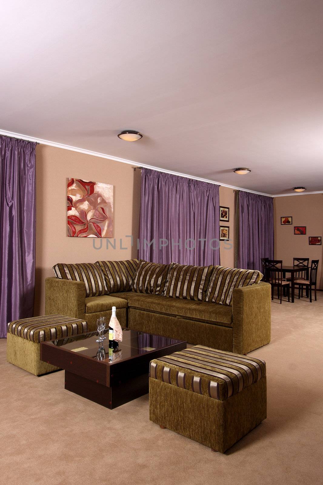 Interior of a modern living room with a convenient sofa, a small little table for drinks, lilac portieres at windows and a soft carpet covering on a floor