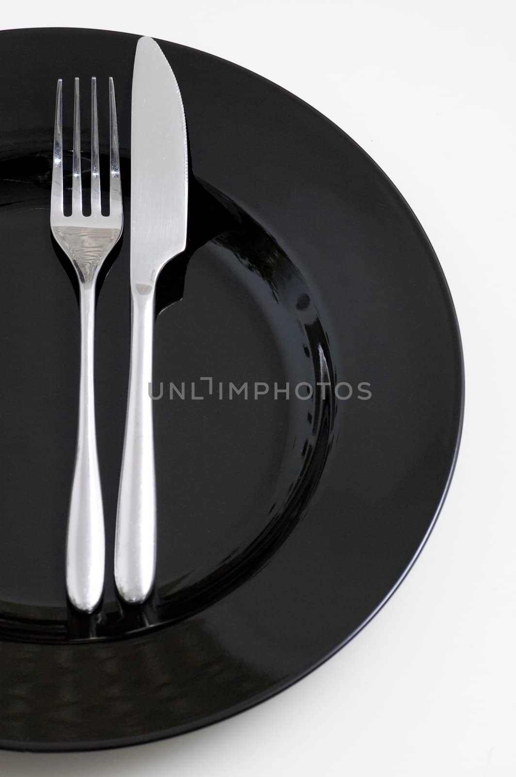 steel fork and knife on a black ceramic saucer isolated on white