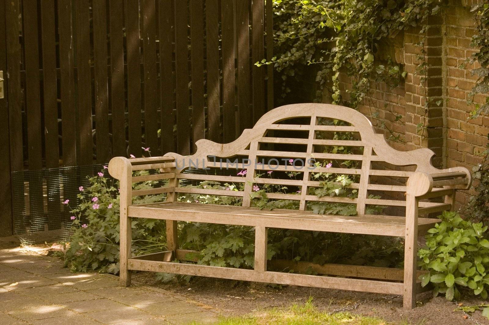 Wooden garden bench in shadow of a park wall