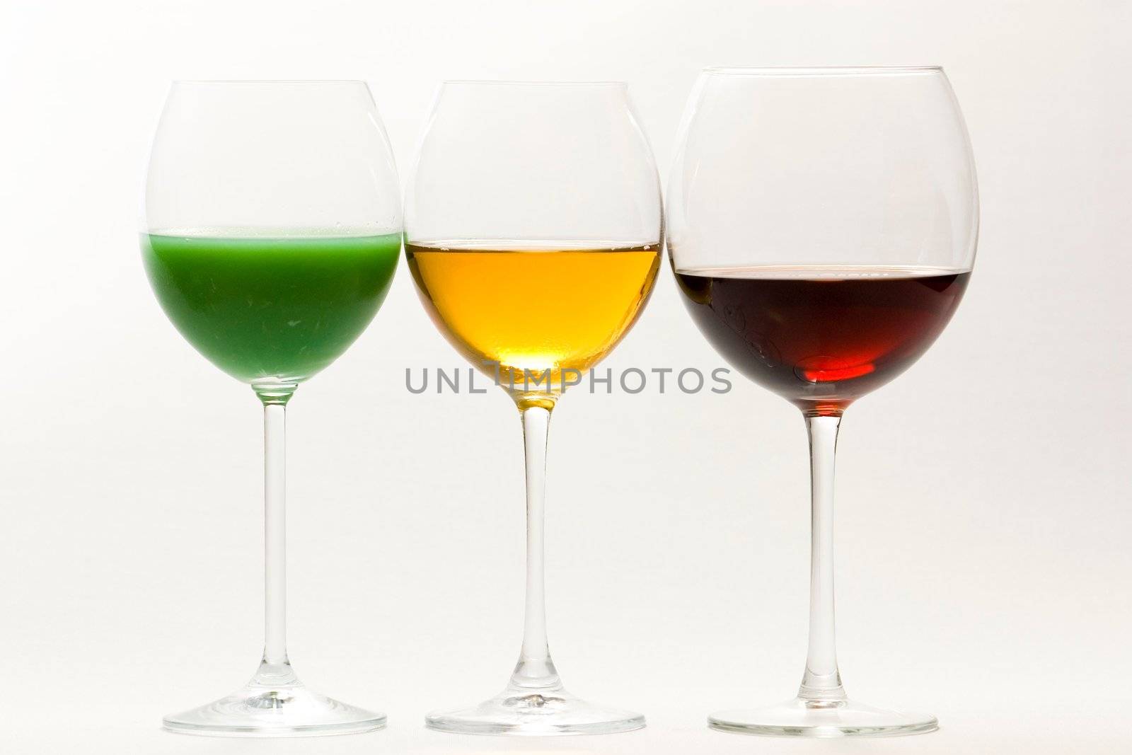 Three tall glasses on white background filled with: white, red wine and green cocktail