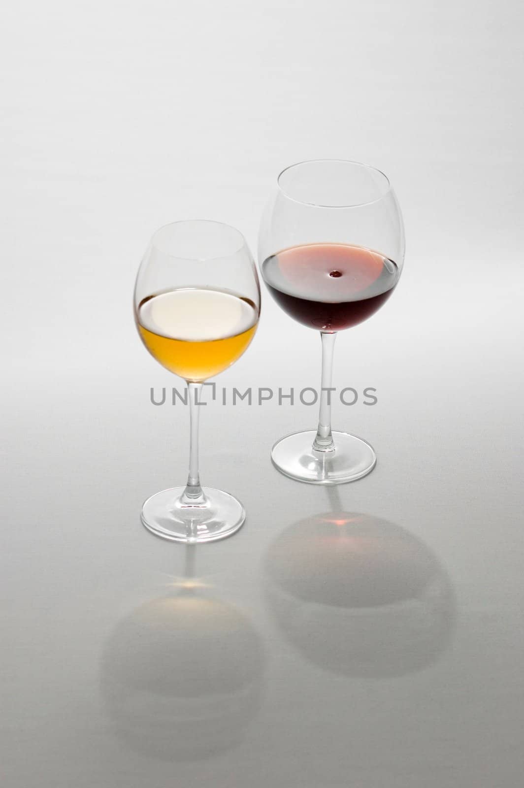 Two tall glasses on light background filled with red and white wine