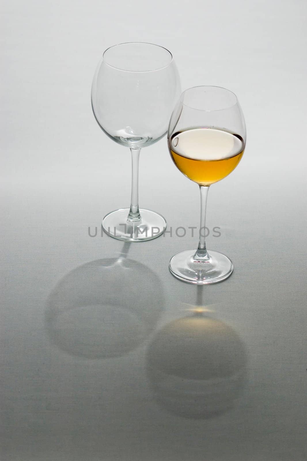 Two tall wine glasses on light background, one filled with white wine