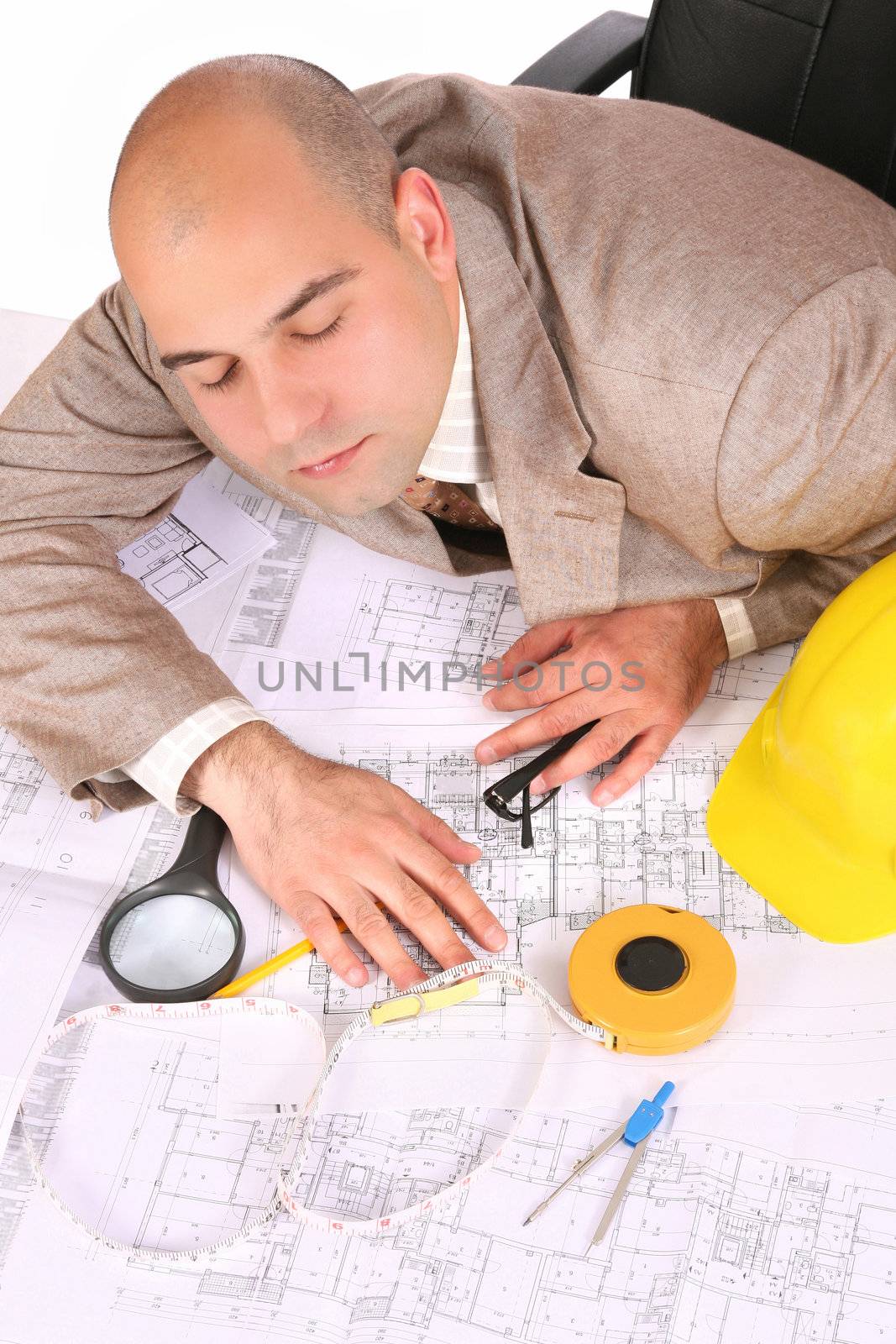 A businessman sleepy with architectural plans at desk