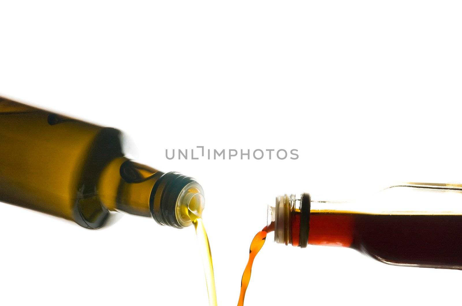 Olive oil and vinegar being poured from bottles isolated on white