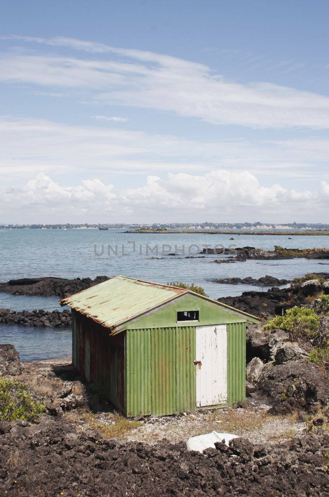 A weathered boat shed sits on the rocky shore of Rangitoto Island, Hauraki Gulf, New Zealand