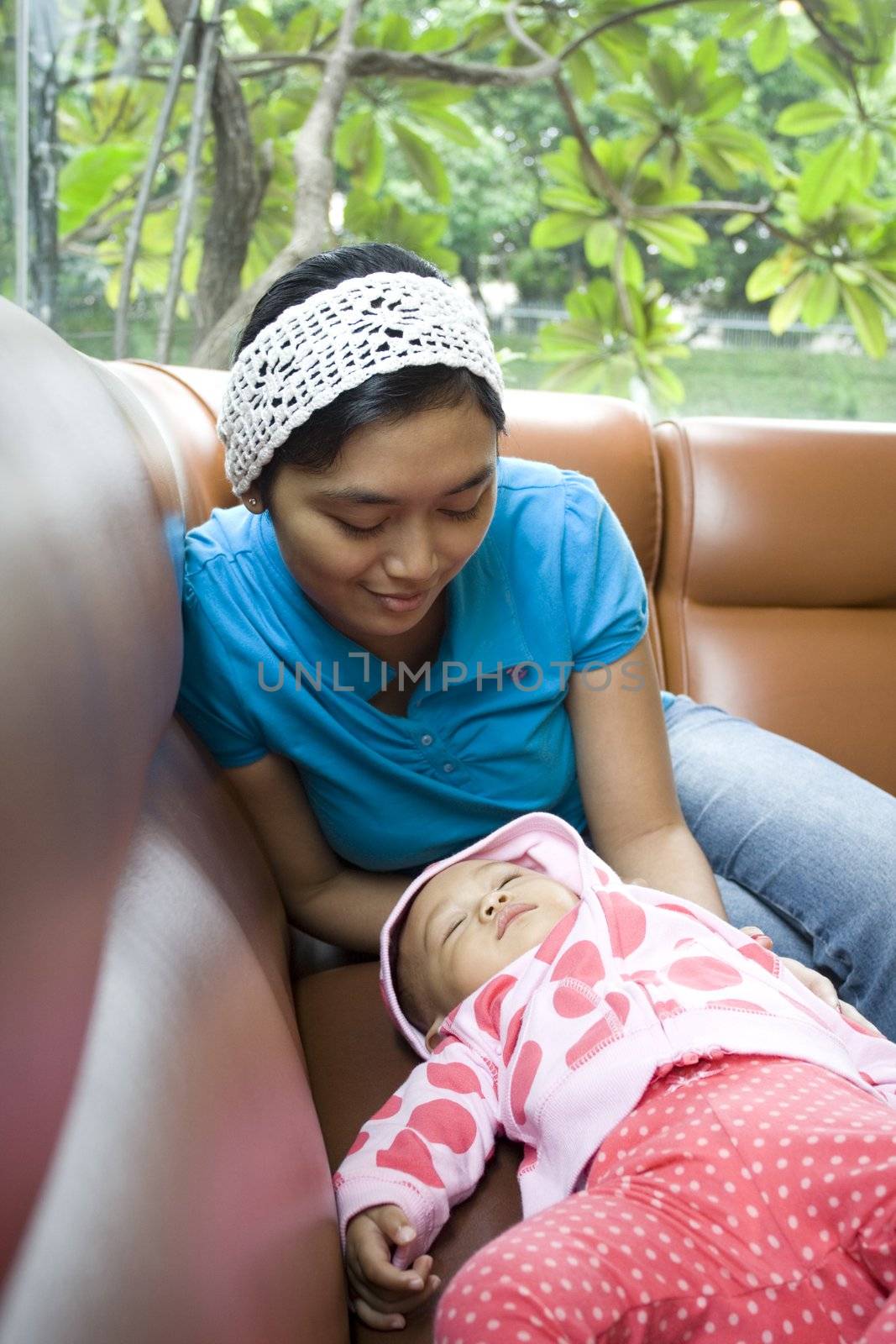 photo of a baby fall a sleep on a sofa, mother is looking after lovingly