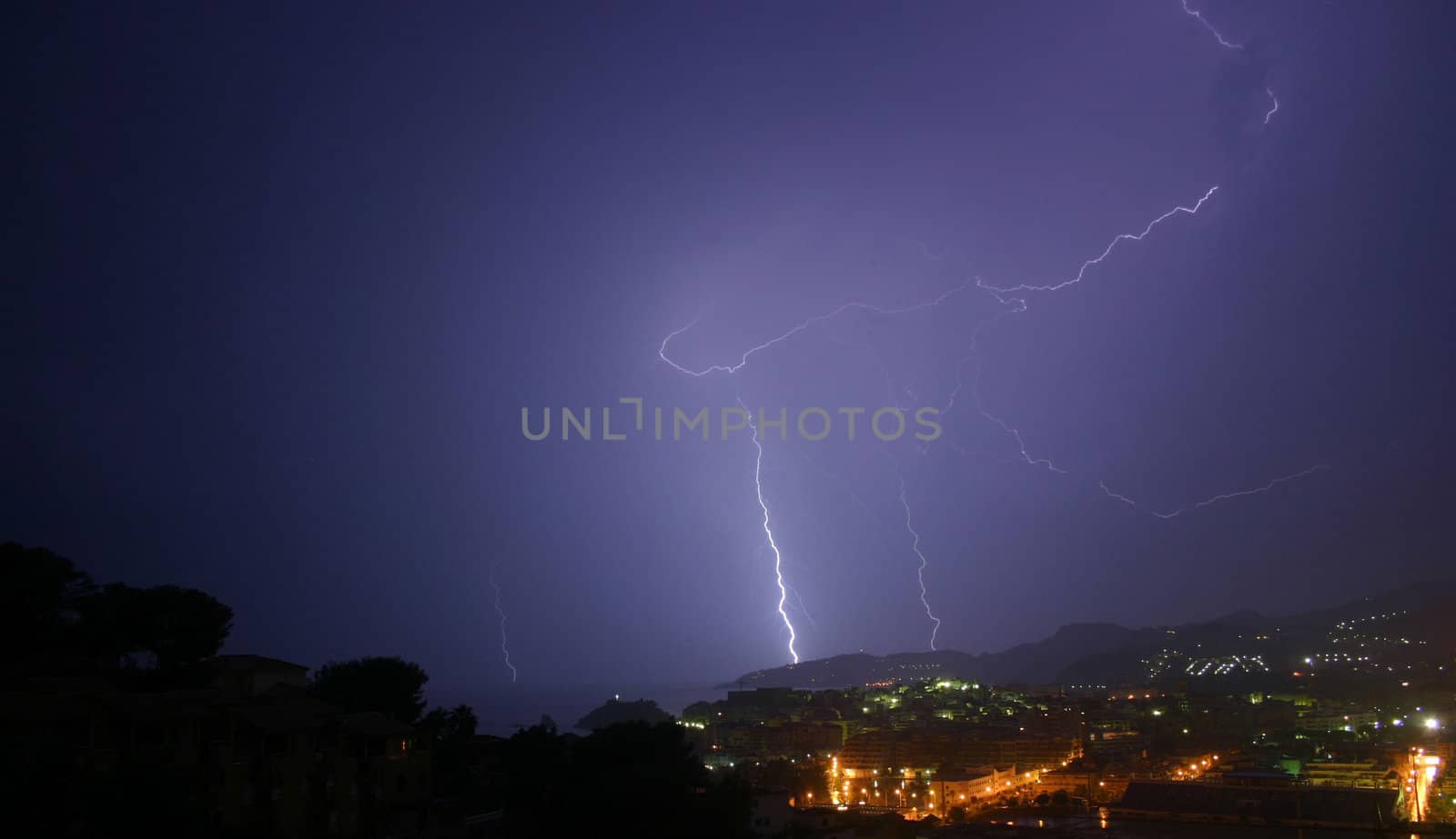 3 lightning photos shot from the same viewpoint.  Same landscape, choice of bolts.  The image is taken from a high viewpoint, overlooking trees, a town and mountains.  This is my favourite of the 3 because of the almost 'batman'-like lighting and colour
