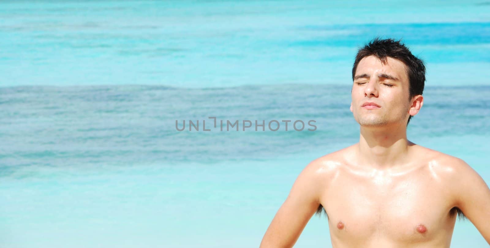 wide photo of a handsome man sunbathing at a tropical beach (ocean background)