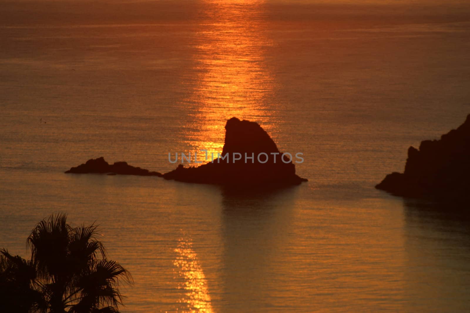 An almost impressionist view of a rock at sea backlit by the reflection of the setting sun.