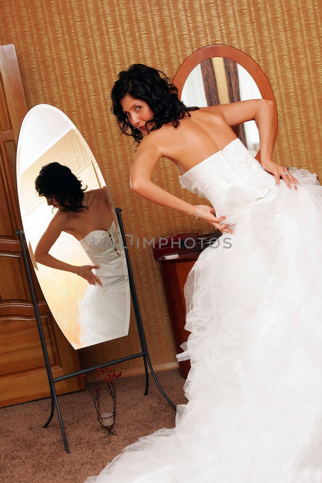 Rear view of bride trying on wedding dress and looking in mirror.