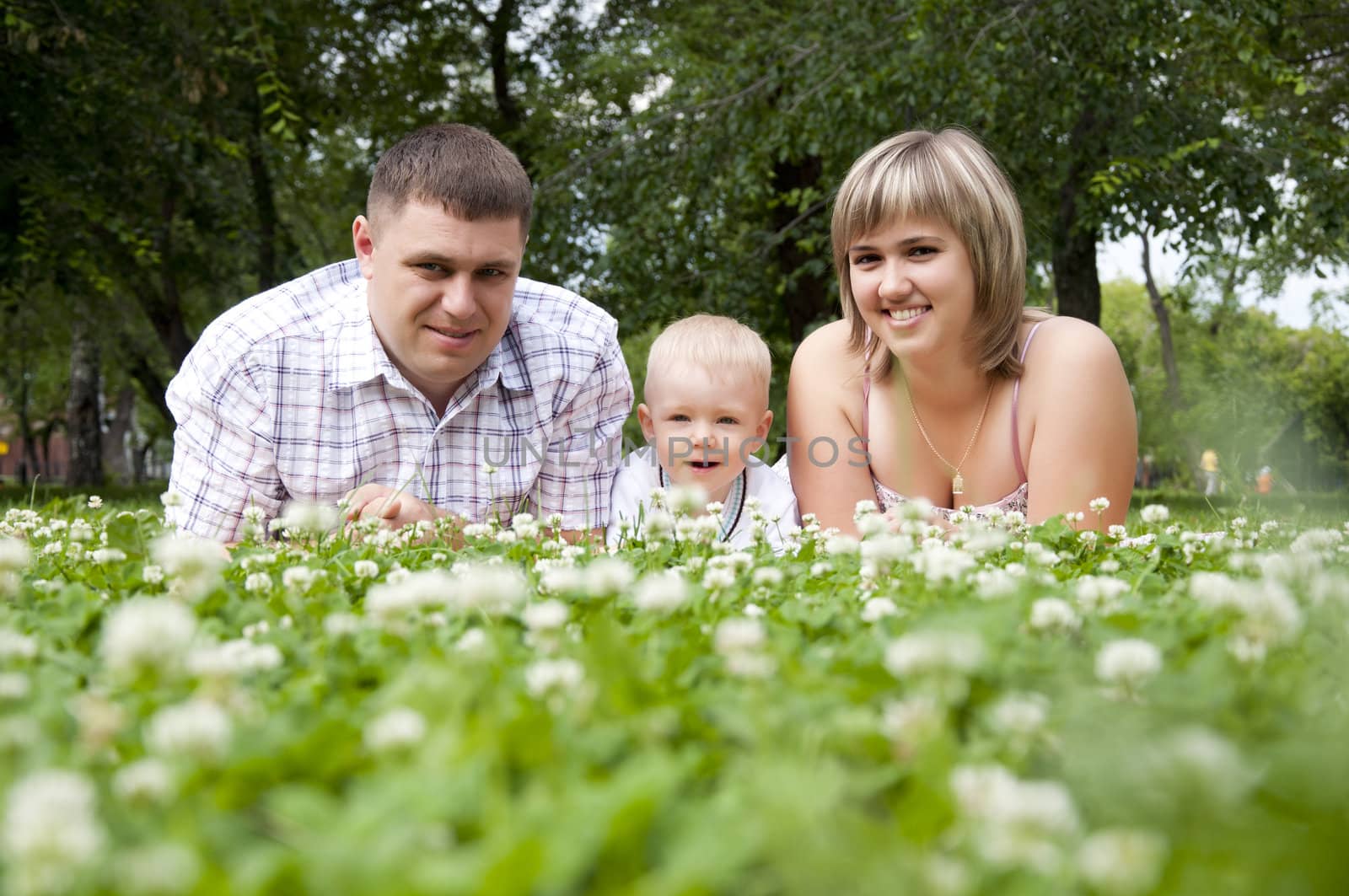 The young family in park, lays on a grass and smiles