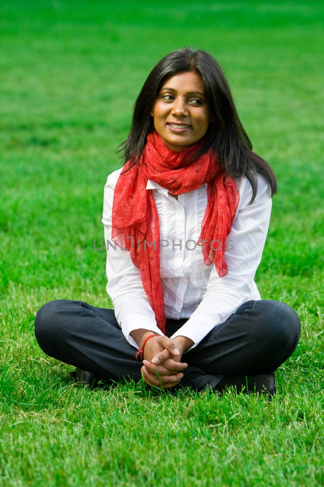 Pretty young indian girl sitting on the grass at a park