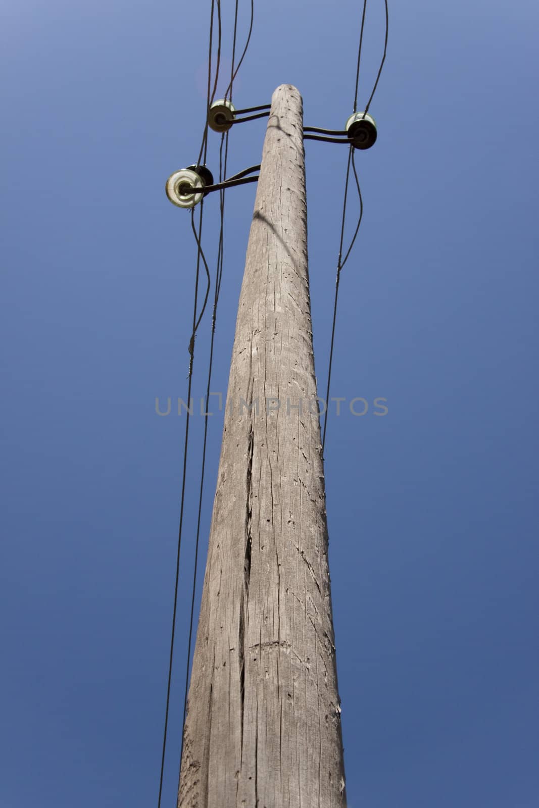 Old one wooden pillar with power line, blue sky.