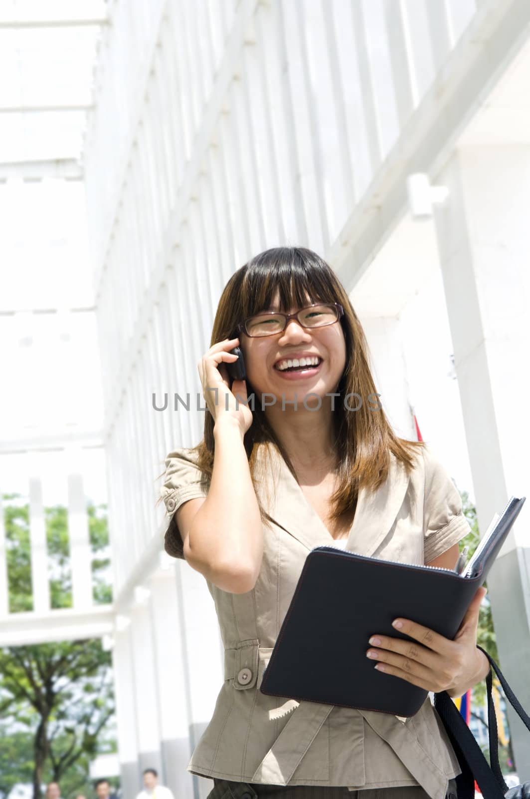 Asian Businesswoman on the phone with diary walking outside office building, motion blurred.