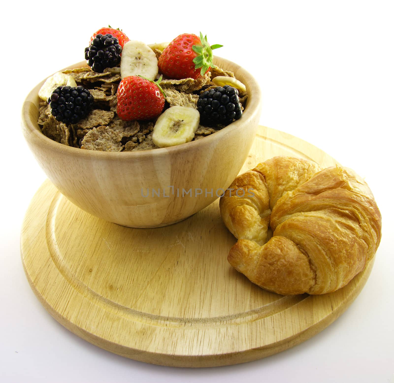 Crunchy looking delicious bran flakes and juicy fruit in a wooden bowl with a croissant on a white background