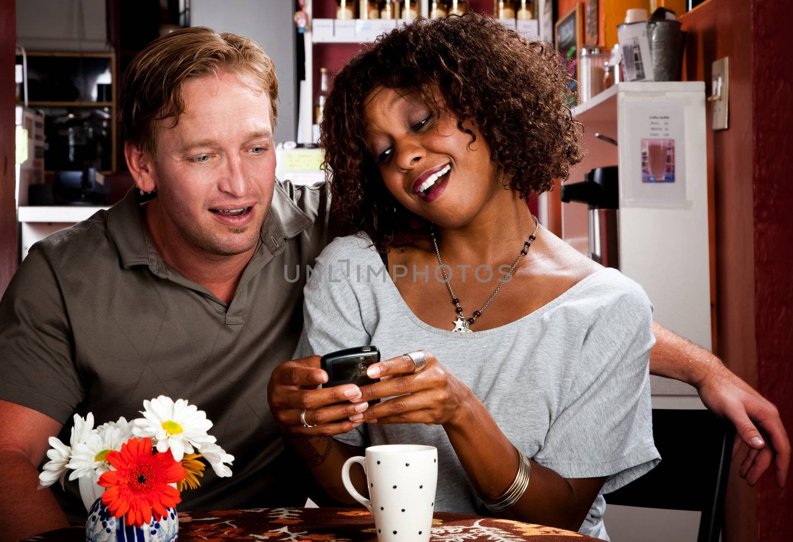 Mixed race couple in coffee house with cell phone by Creatista
