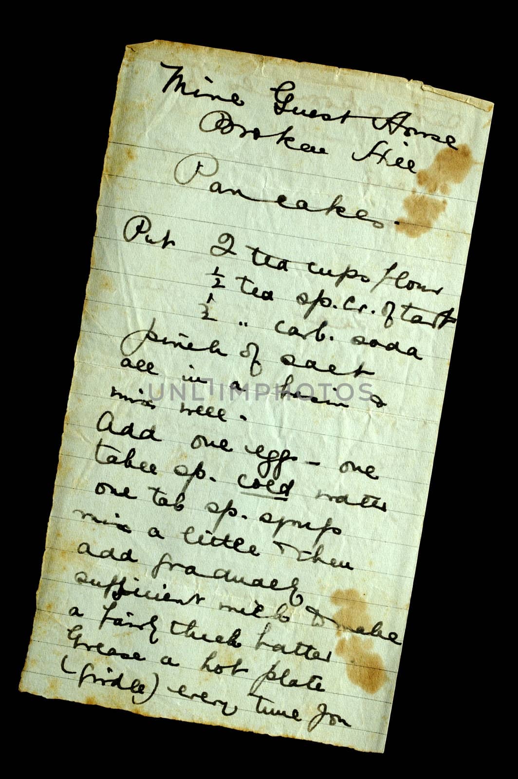A hand-written recipe for pancakes, on stained and crumpled paper, isolated on black. Found in a 100-year old cookery book.