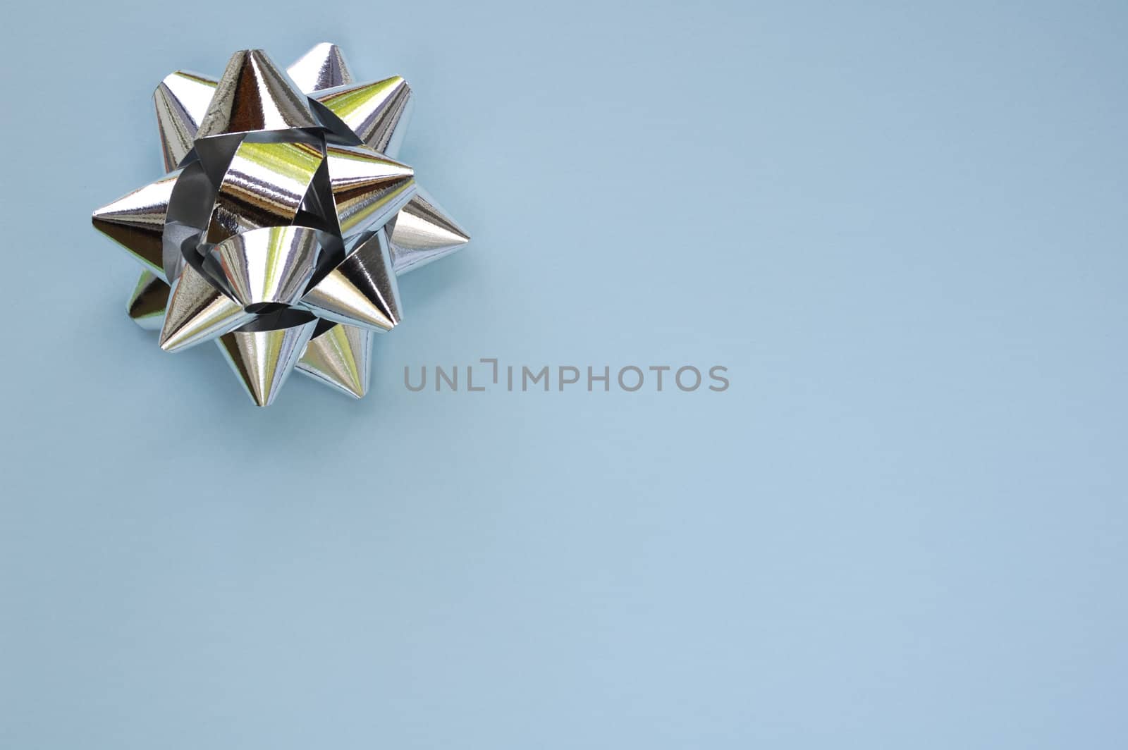 A decorative star, made from silver ribbon, on a plain, pale blue background with space for text (copy).
