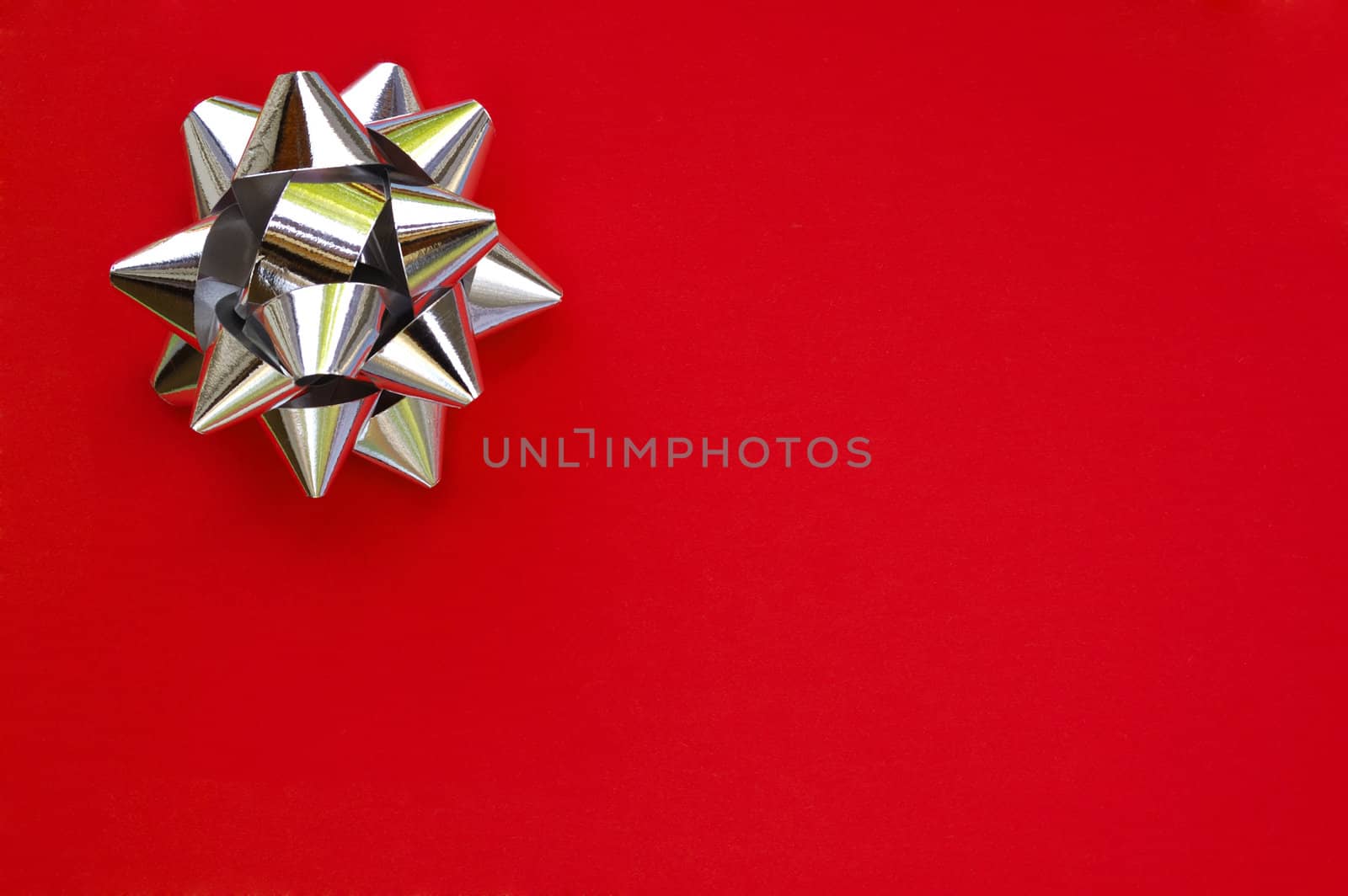 A decorative star, made from silver ribbon, on a plain red background with space for text (copy).