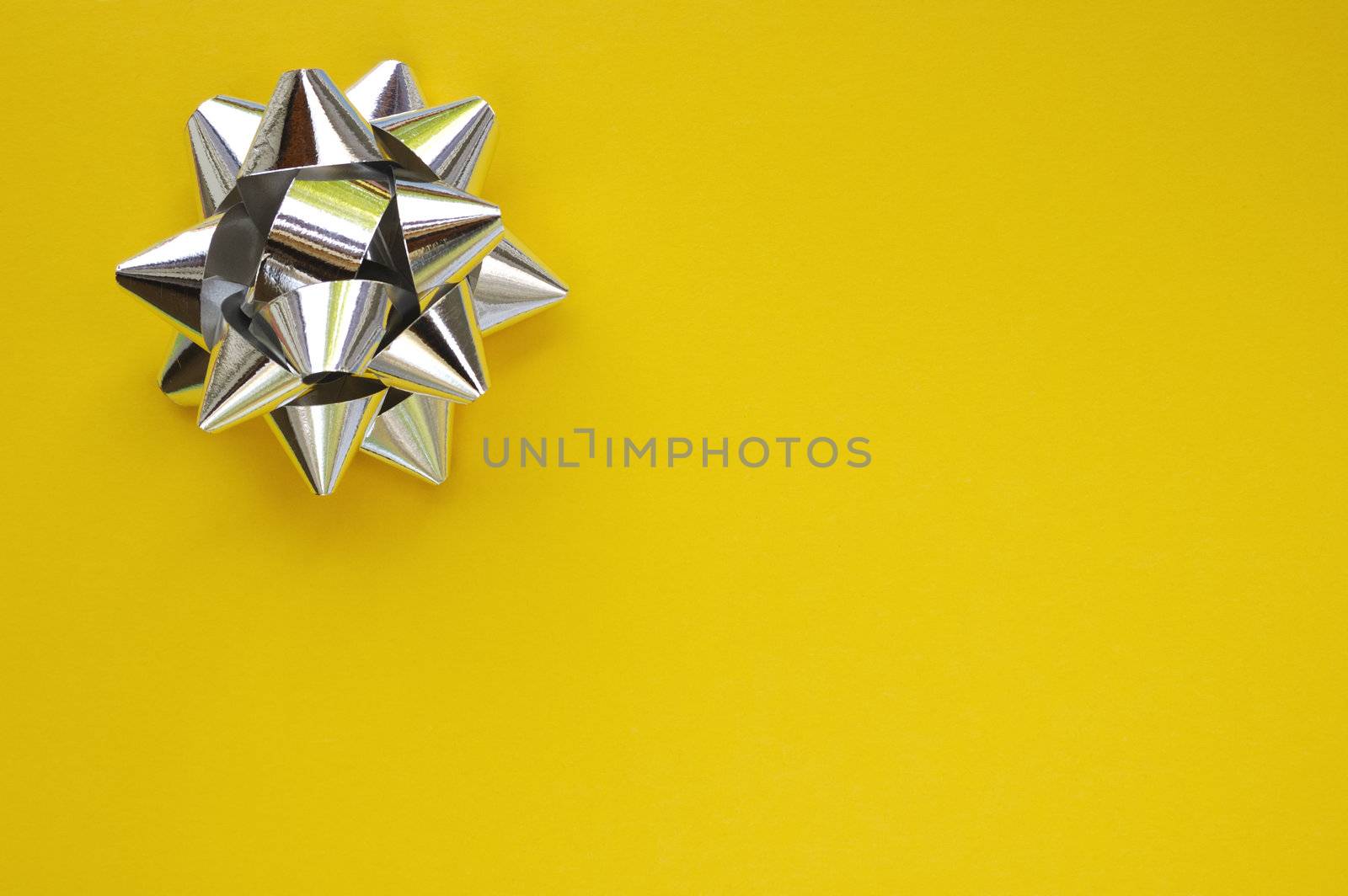 A decorative star, made from silver ribbon, on a plain yellow background with space for text (copy).