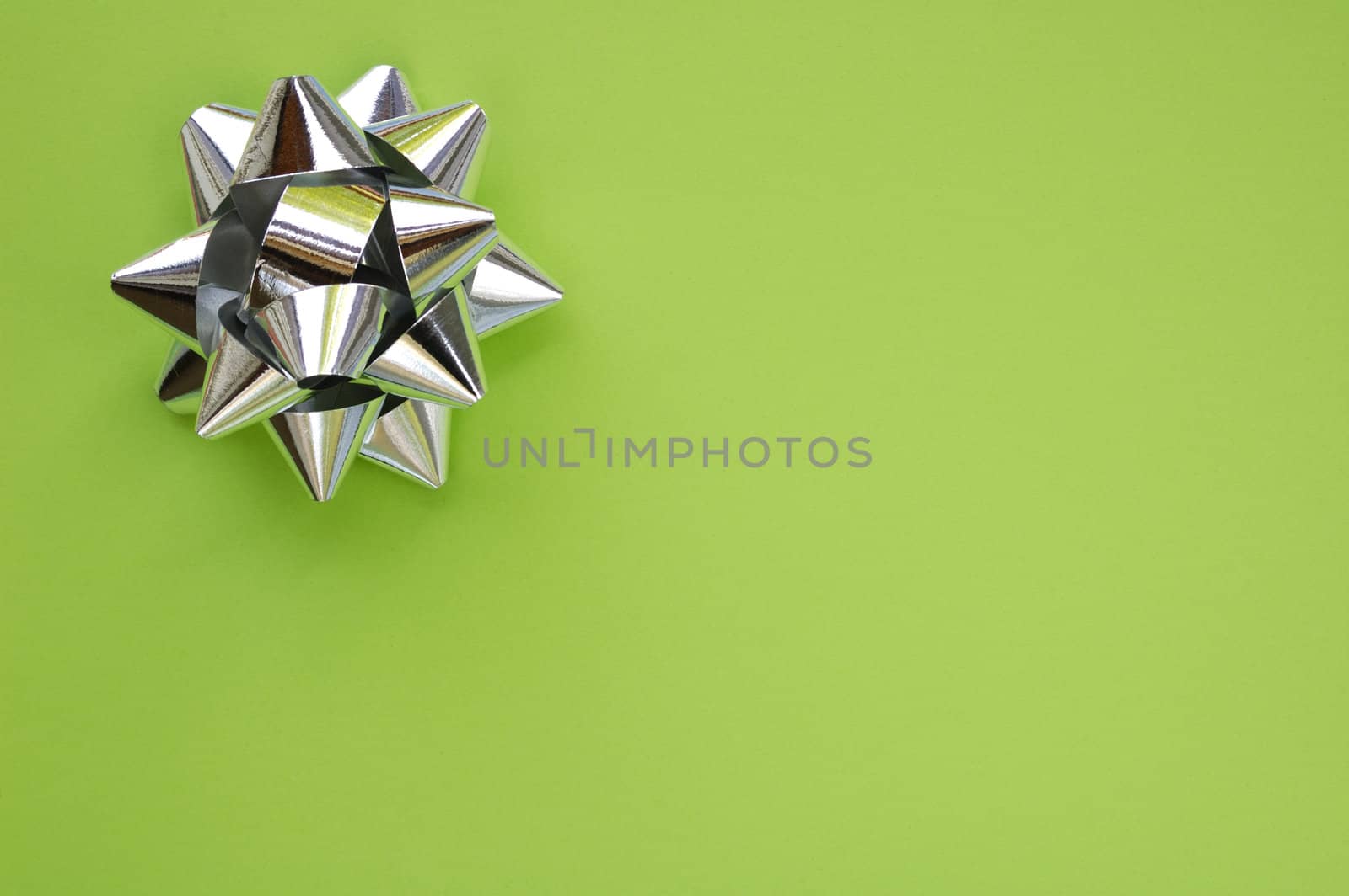 A decorative star, made from silver ribbon, on a plain green background with space for text (copy).