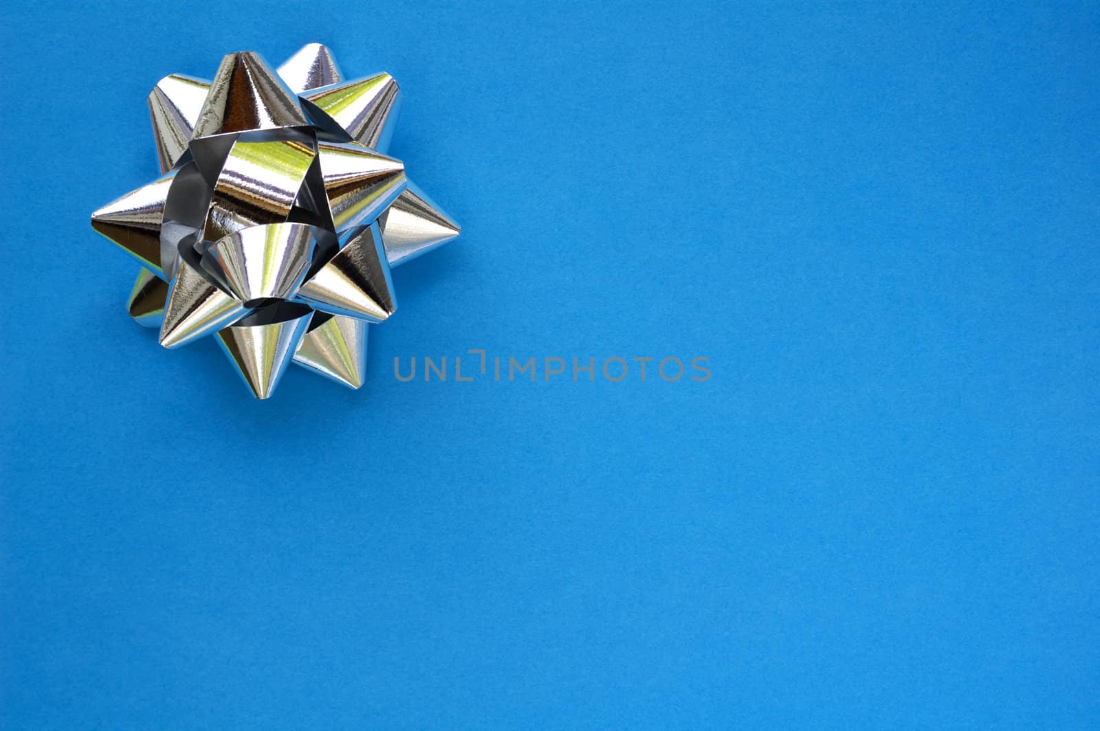 A decorative star, made from silver ribbon, on a plain blue background with space for text (copy).