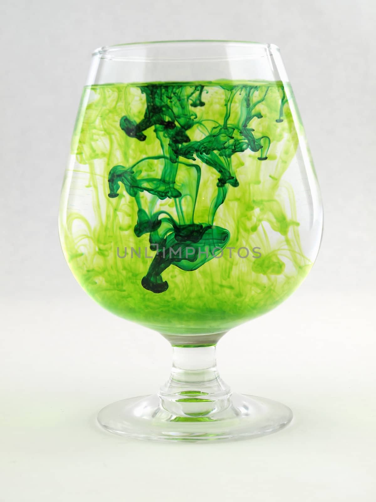 A liquid filled glass with green swirls over a white background.