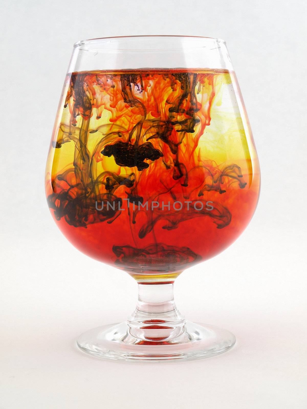 A liquid filled glass with black, red and yellow swirls over a white background.