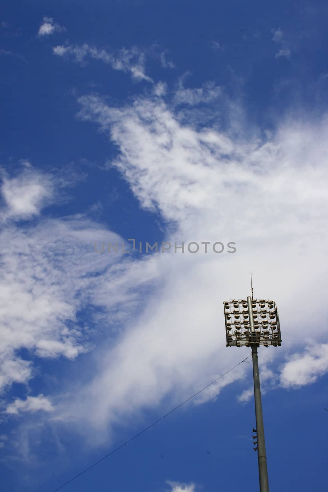 Blue sky and white clouds and a stadium spot light post at right hand corner.