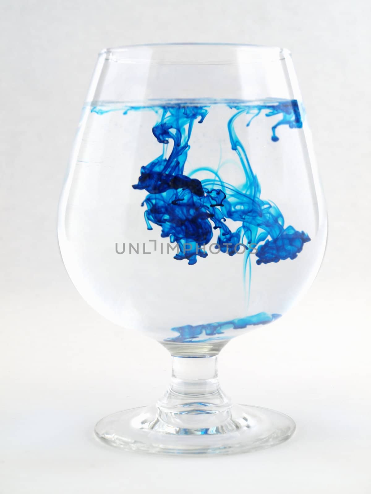 A liquid filled glass with blue swirls over a white background.
