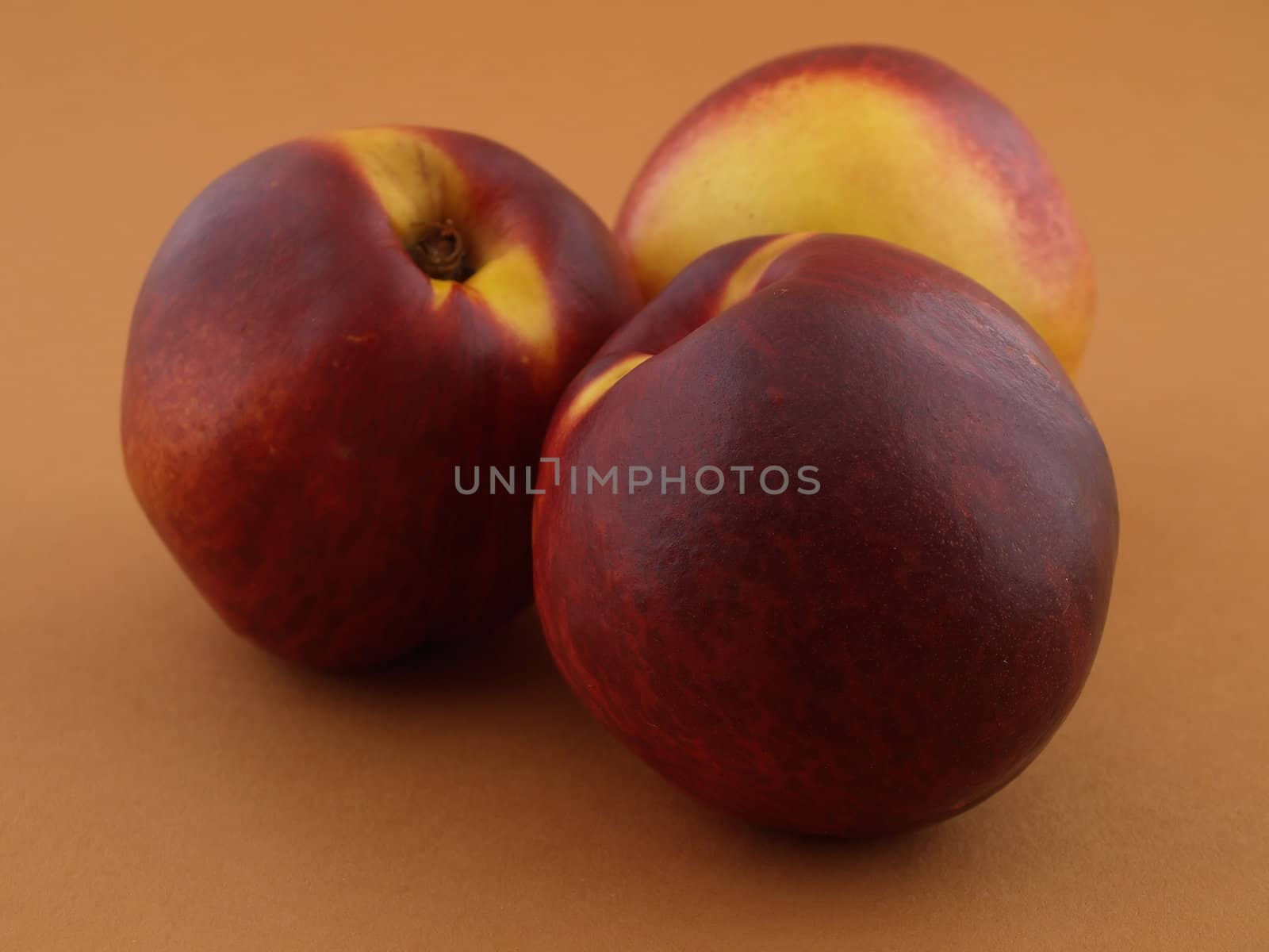 Three ripe peaches on a tan colored background.