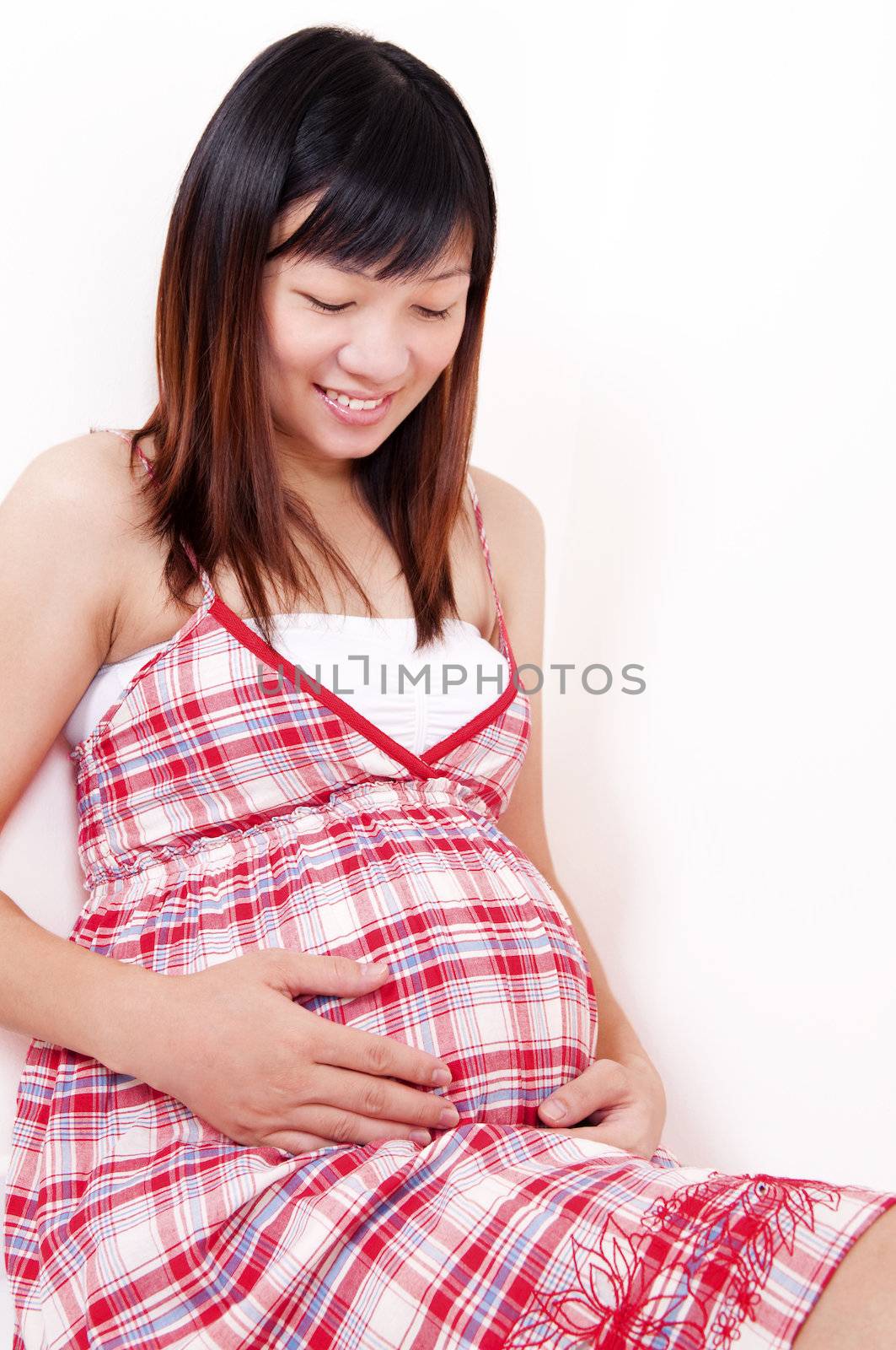 Happy Young Asian Mother looking at her 8 months pregnant stomach.
