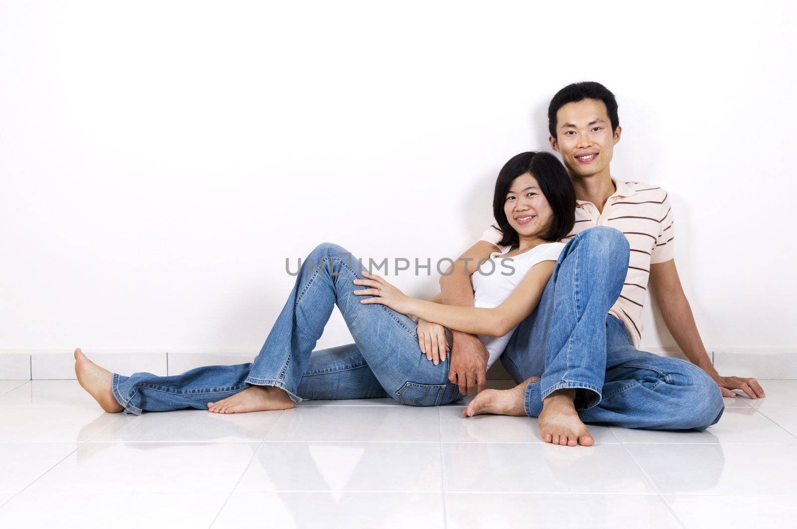 Young Asian adult couple sitting together on tiles floor in home smiling.