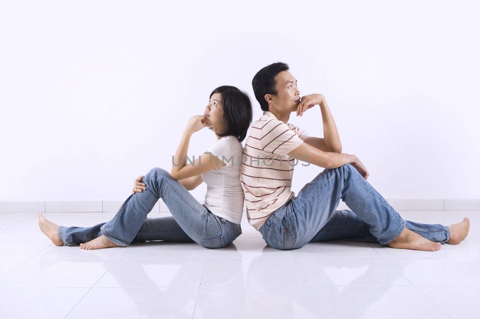Young Asian adult couple sitting together on tiles floor in home having thought.
