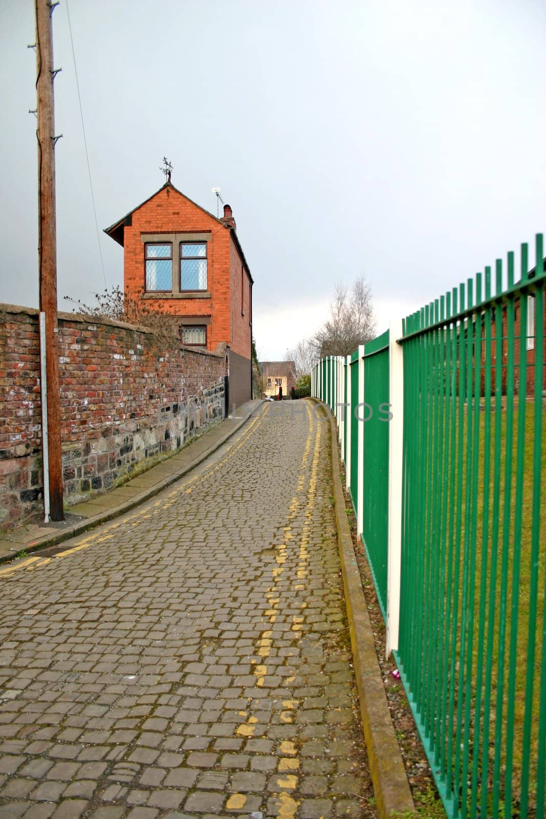 Narrow Cobbled Lane Running Between Metal Fence and House Wall