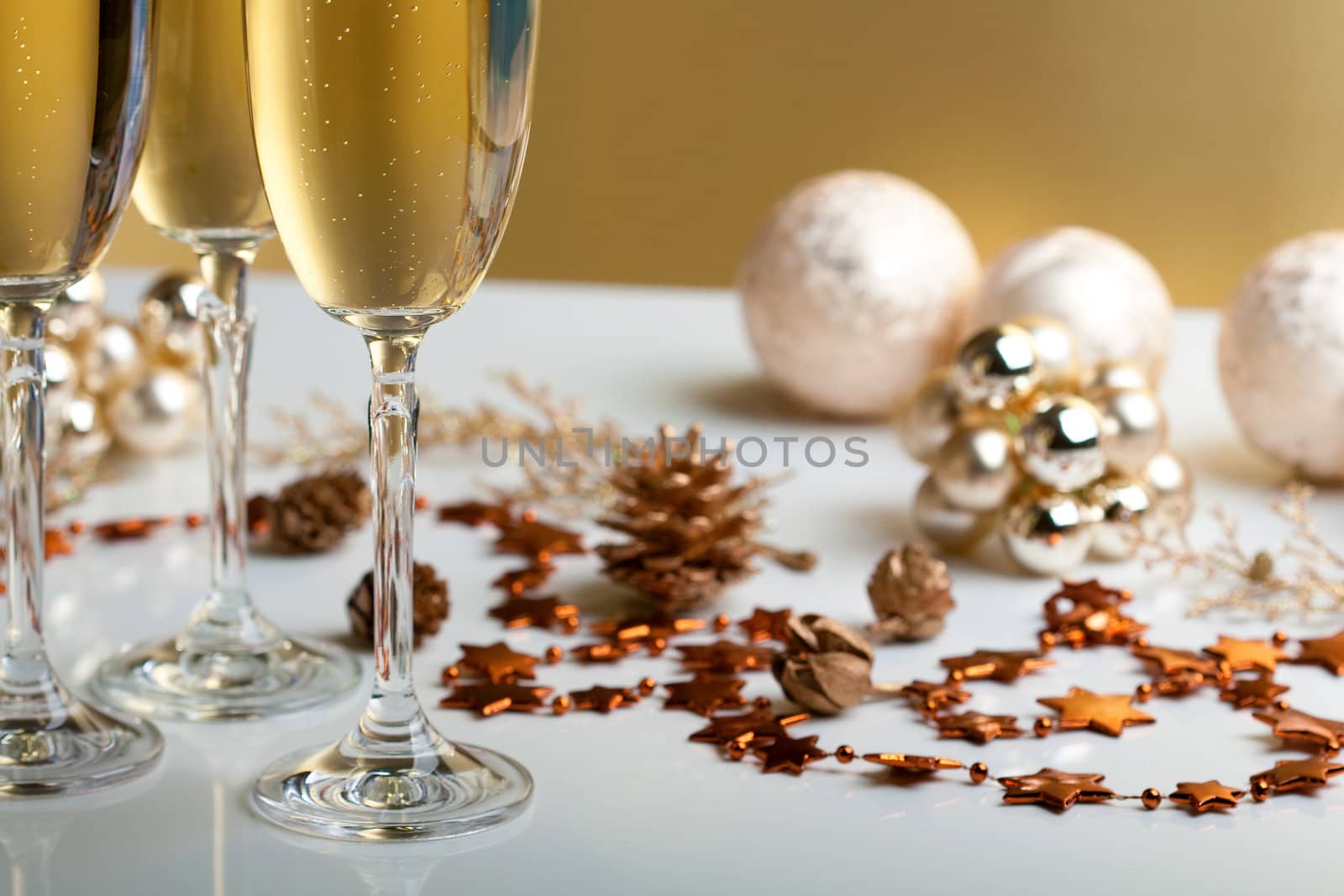 three glasses of champagne, christmas balls and ornaments in front of golden background