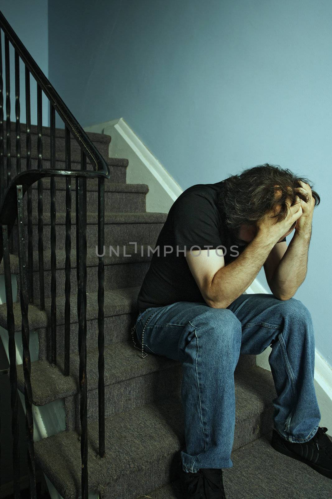 Depressed adult male sitting on stairs. Cross-processed and darkened for moody look.
