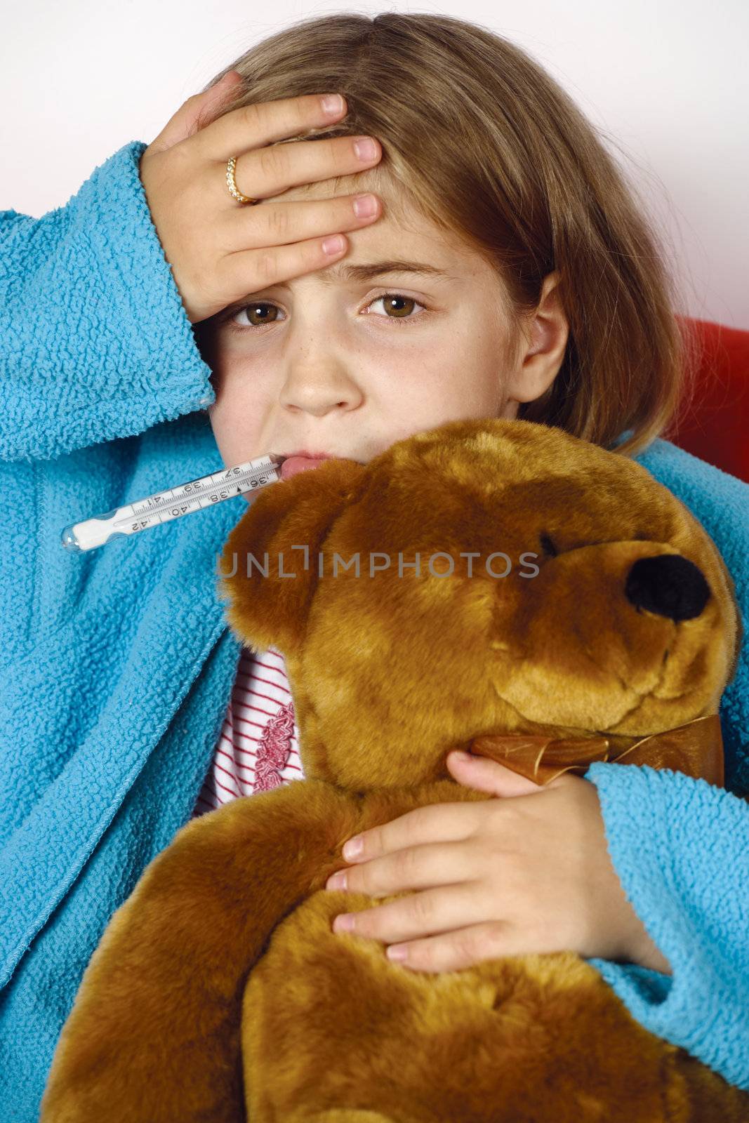 Sick child with thermometer in her mouth, a hand on her forehead and clutching a stuffed animal.