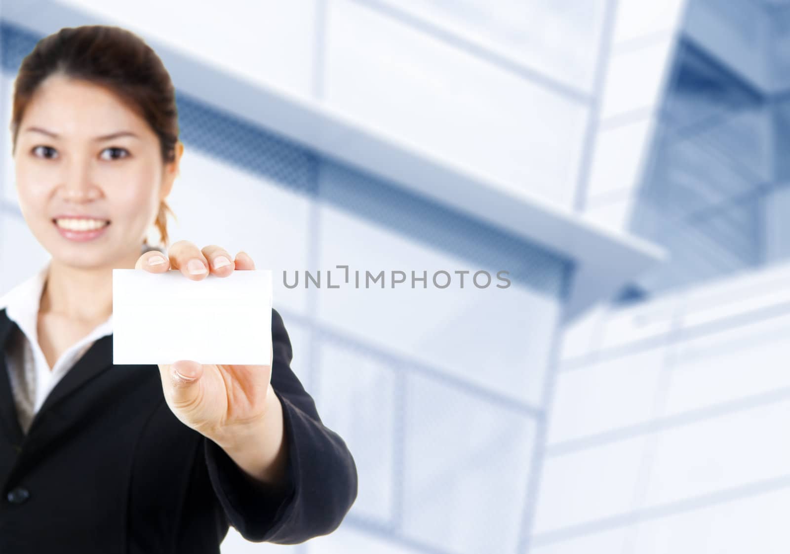 Young Asian with blank business card in a hand, office building as background.