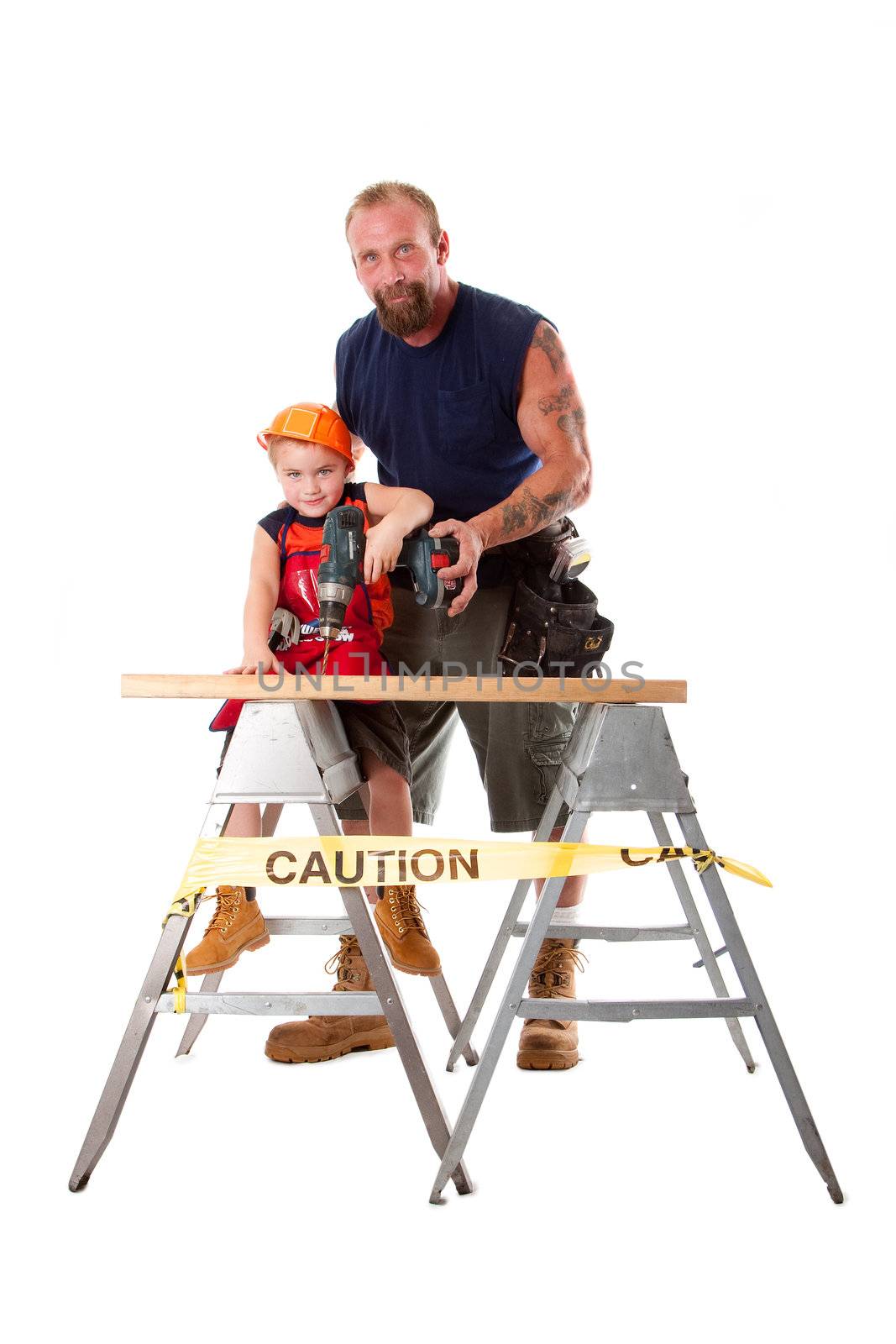 Caucasian dad is teaching cute son with construction helmet how to drill a hole in a wooden plank, isolated.