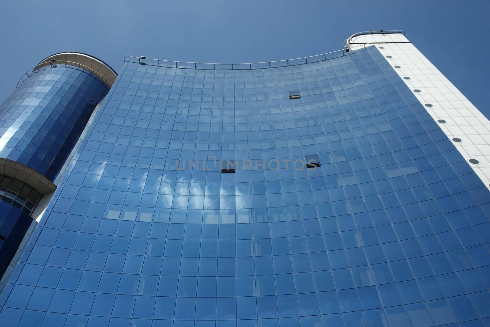 Dark blue, big, high building in which windows clouds were reflected.