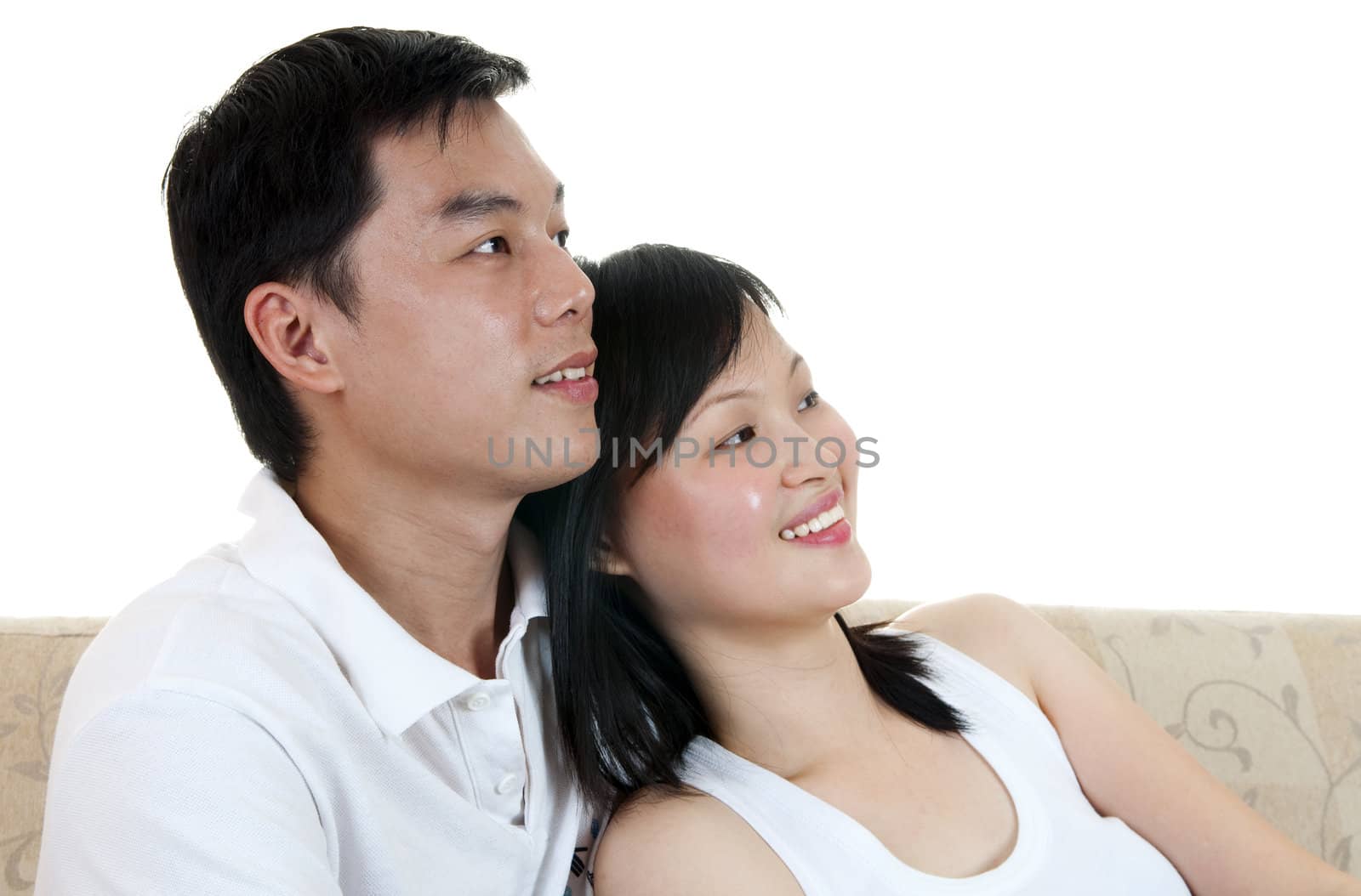 Asian couple sitting on sofa and looking at side.
