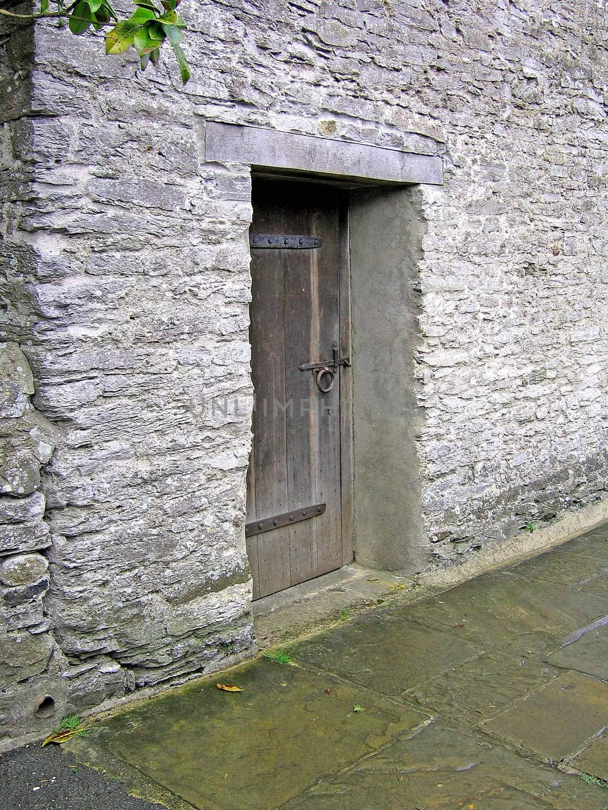 Old wooden door, set against a thick stone wall on a path near Buckfast Abbey in Devon, England