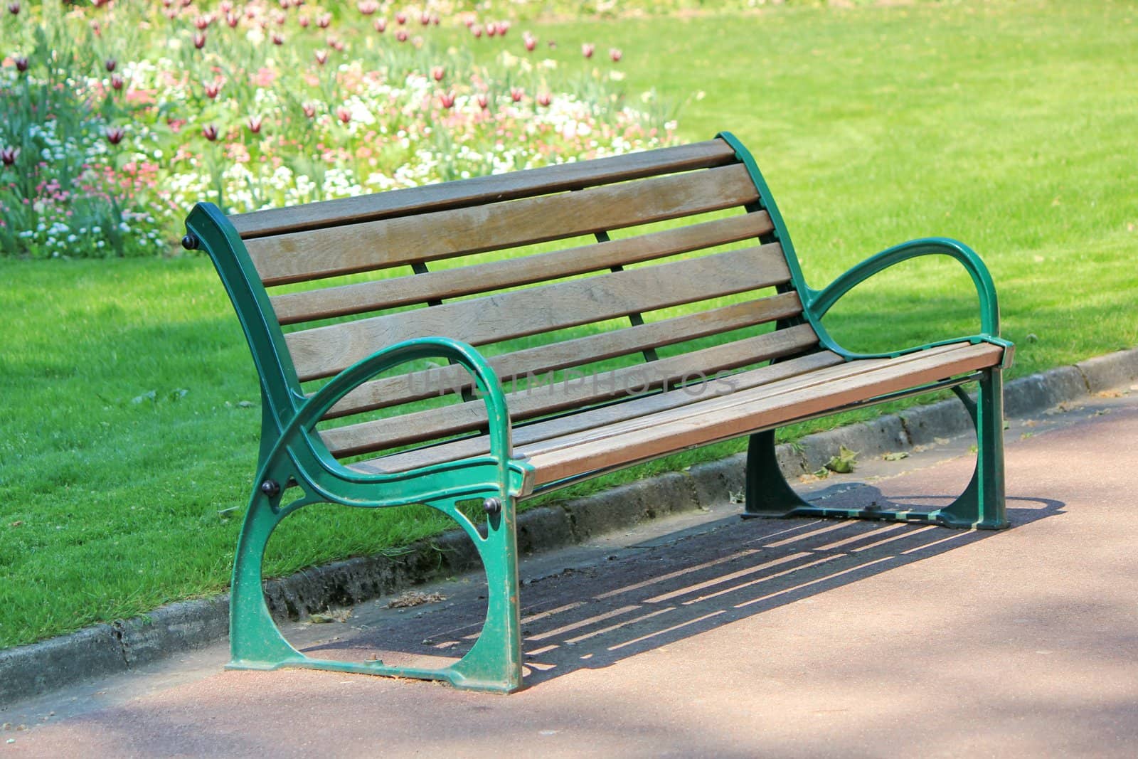 Green and brown wood bench in a park with grass and flowers behind