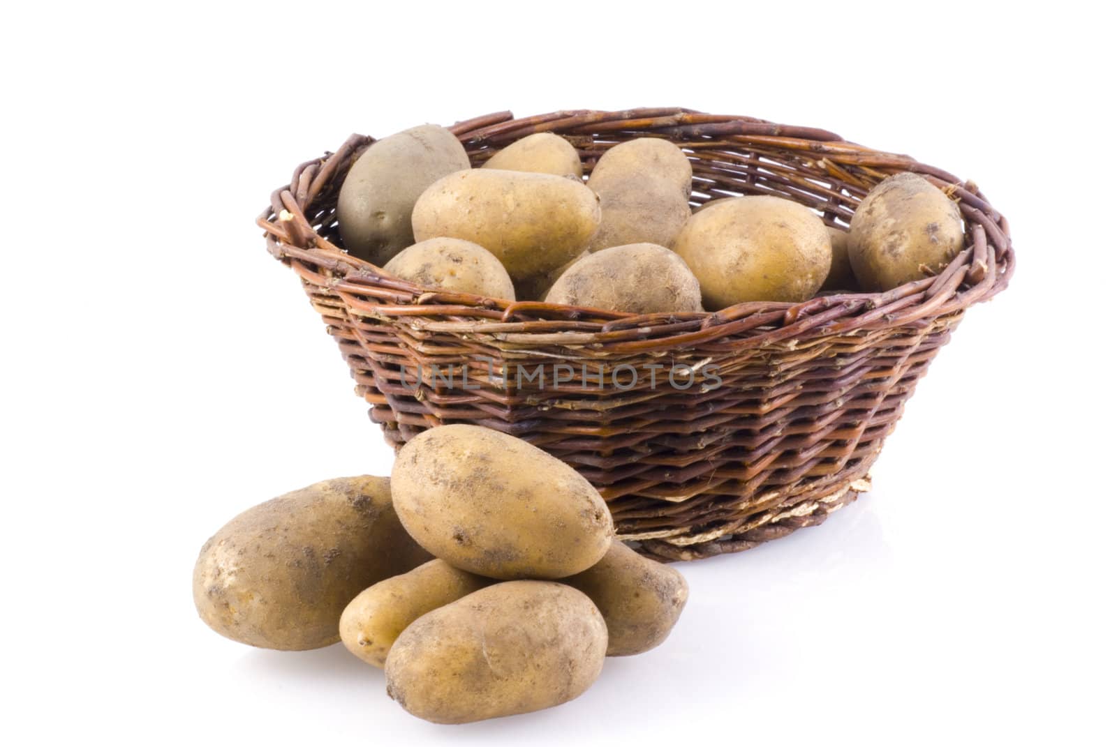 Basket full of potatoes, with a few next to it, isolated on white.